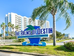 Schild für 'The Palms of Destin' mit blaugrünem Design, Palmen und einem weißen Gebäude im Hintergrund.