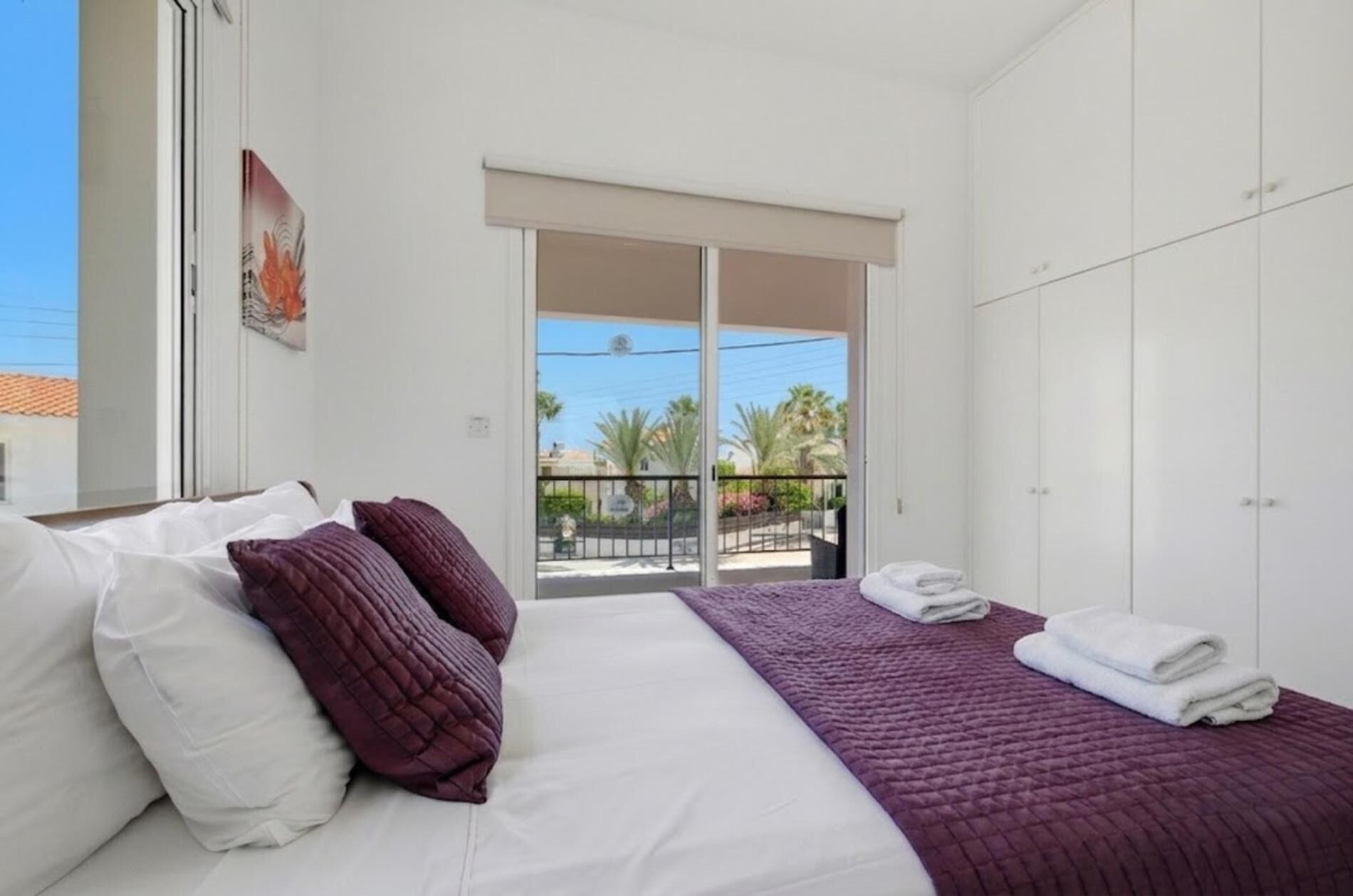 A bedroom with a bed, pillows, a balcony with a view, and a wardrobe.