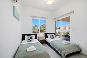 Ein Schlafzimmer mit zwei Betten, einem Fenster, einem Nachttisch und einem Balkon.