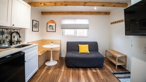 Une cuisine compacte équipée d’un lave-vaisselle, d’une petite table ronde, d’un canapé agrémenté d’un coussin jaune, d’un banc en bois et d’une lucarne au plafond.