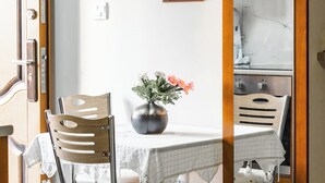 Ruokailutilassa on pöytä, tuoleja, maljakko kukkineen, seinällä oleva kehystetty kuva sekä avoimen oven kautta näkyvä keittiötila.