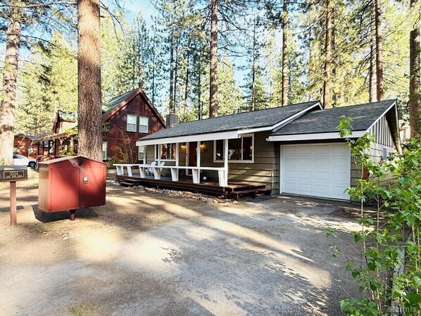 A cabin with a porch, a garage, and a red utility shed in a forested area.