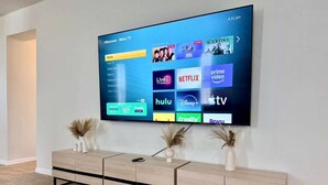 A flat-screen TV mounted on a wall with a wooden entertainment center below. - Stunning 4BR Pool Home Your Private Oasis Awaits (Davenport)