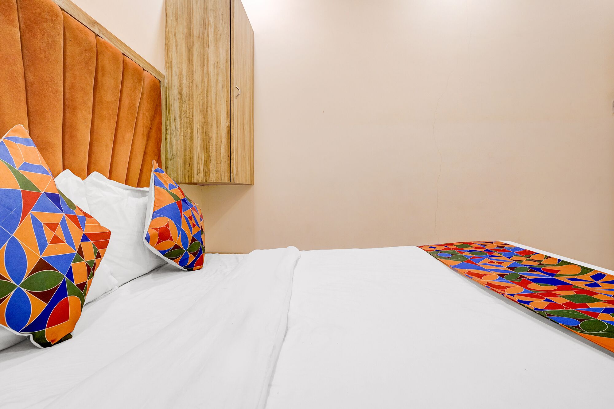 Een bed met witte beddengoed, een houten hoofdeinde en kleurrijke kussens met geometrische patronen.