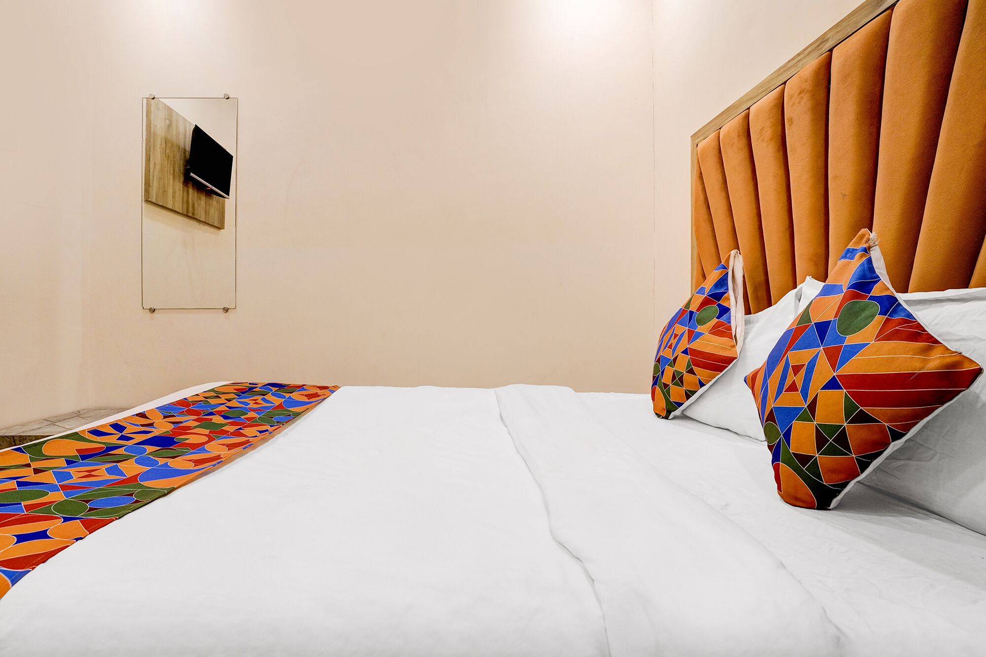 Een net opgemaakt bed met een kleurrijk, geometrisch patroon tapijttekening, een hoofdbord met verticale latten en twee kussens met een geometrisch ontwerp.