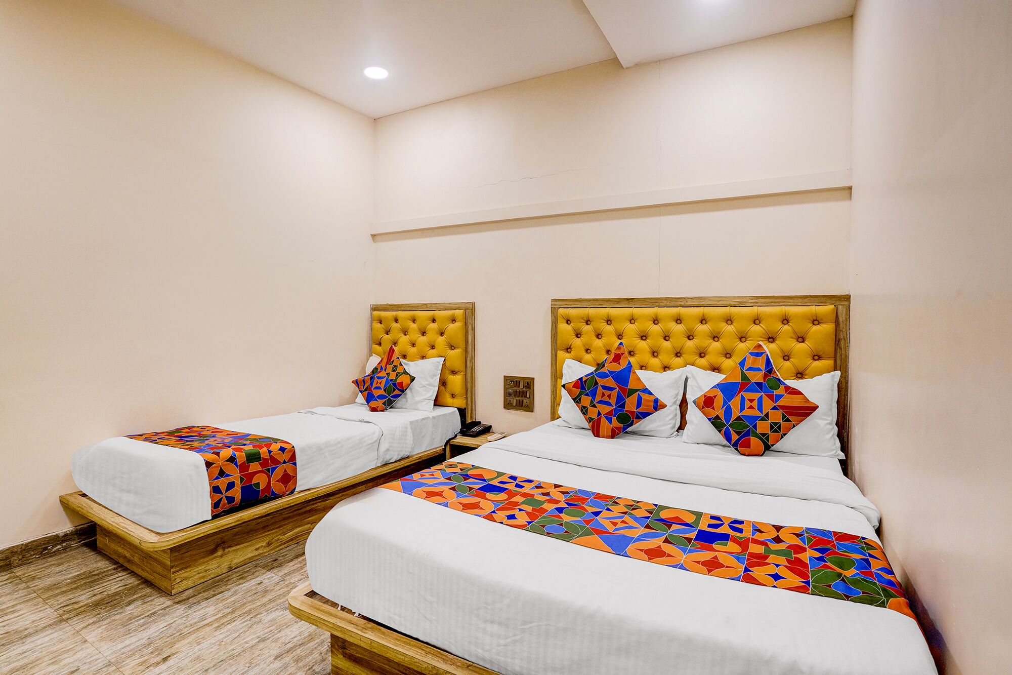 Two beds with yellow headboards, white bedding, and colorful geometric-patterned pillows.