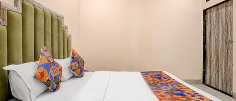 A bed with white bedding, two colorful pillows, and a geometric-patterned bedspread.