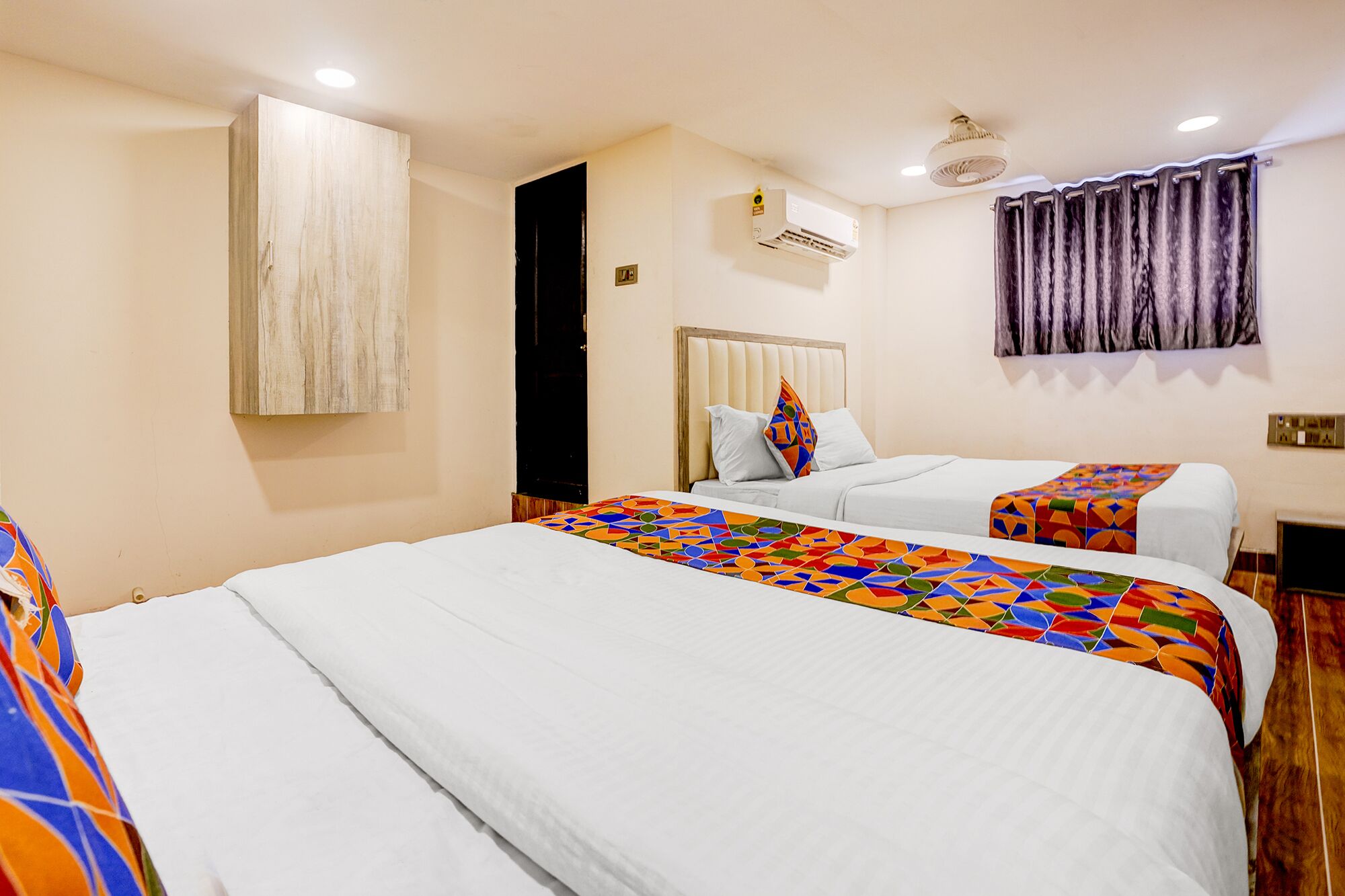 A hotel room with two beds, a wooden headboard, a ceiling fan, and an air conditioning unit.