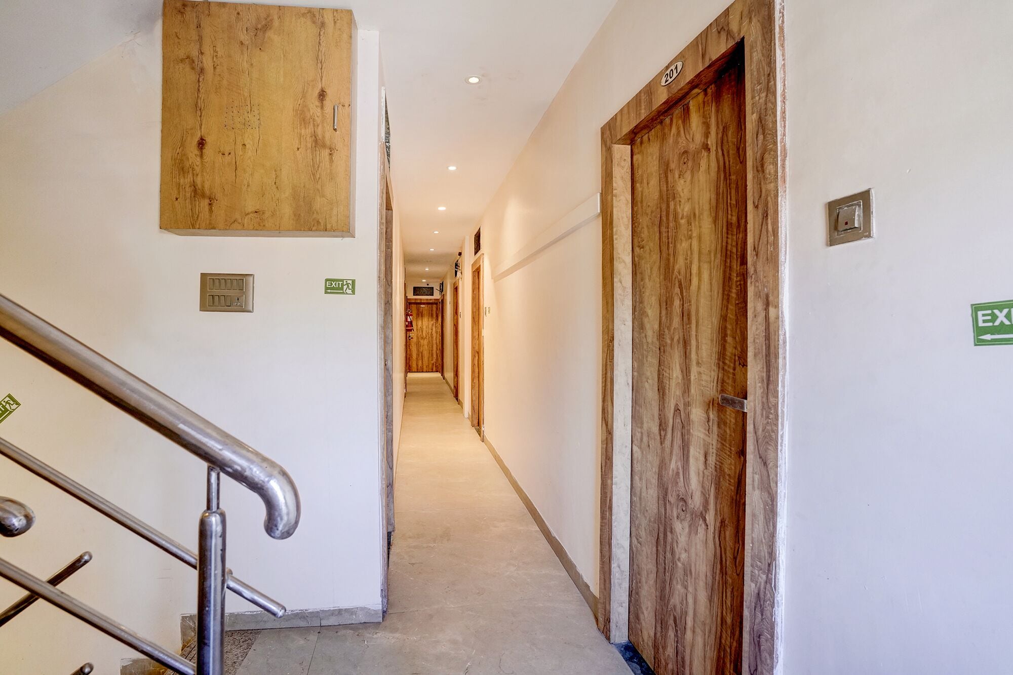 A hallway with wooden doors, an exit sign, and a metal railing.