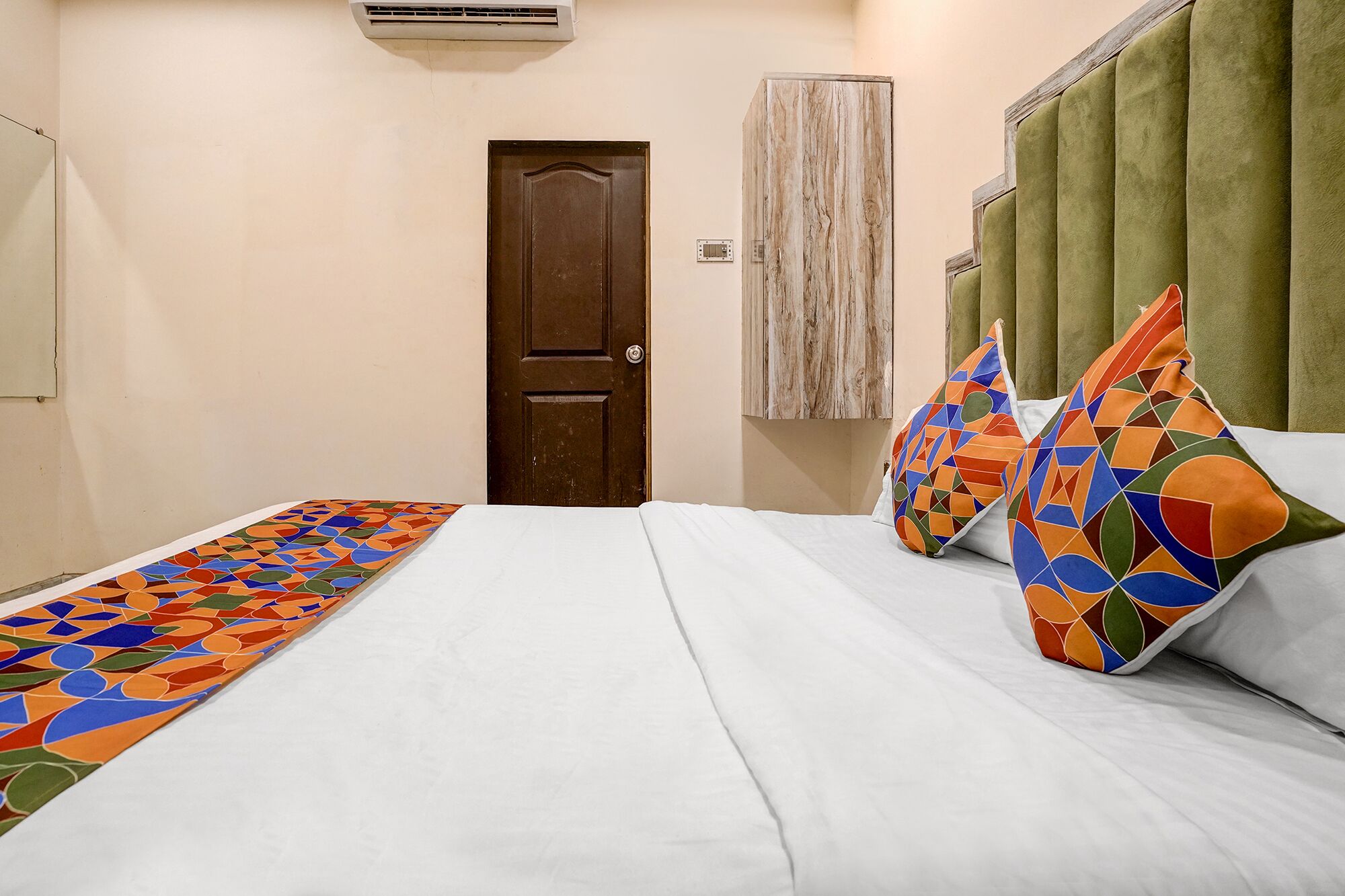 A hotel room with a bed, pillows, a door, and an air conditioning unit.