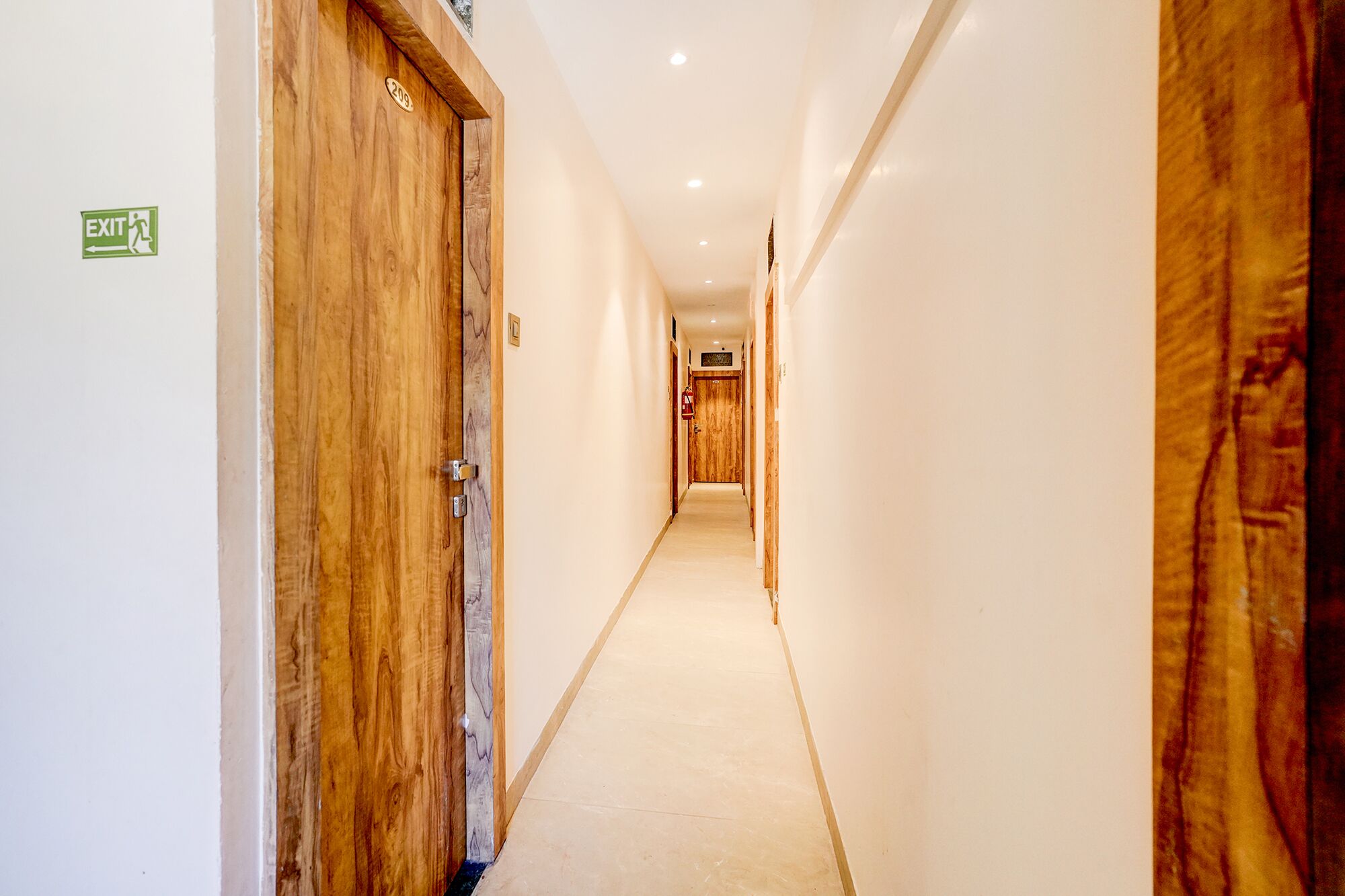 A corridor with wooden doors, a visible exit sign, and a hallway leading to another room.