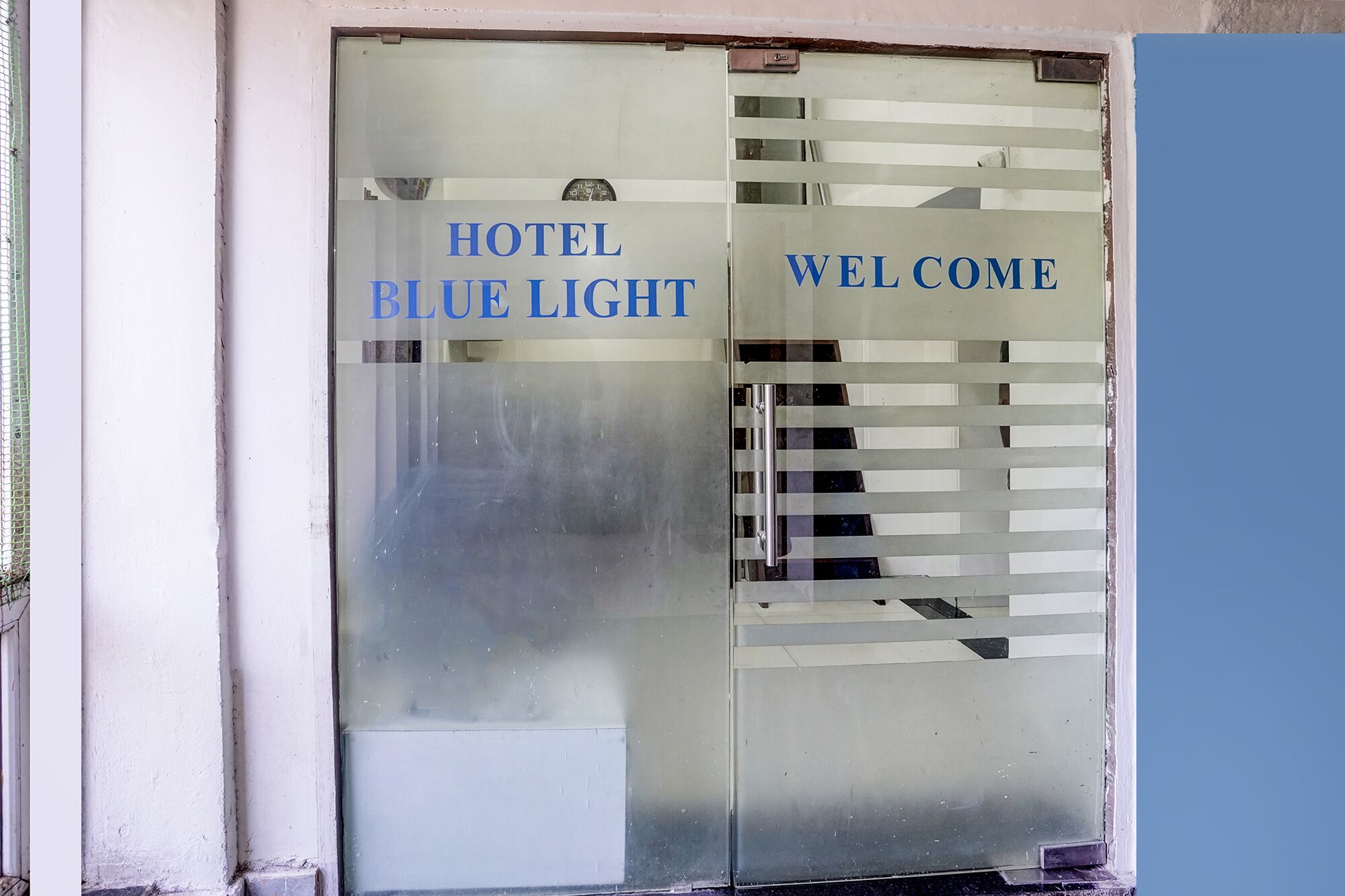 A hotel entrance with a frosted glass door, the words 'HOTEL BLUE LIGHT' and 'WELCOME' visible.