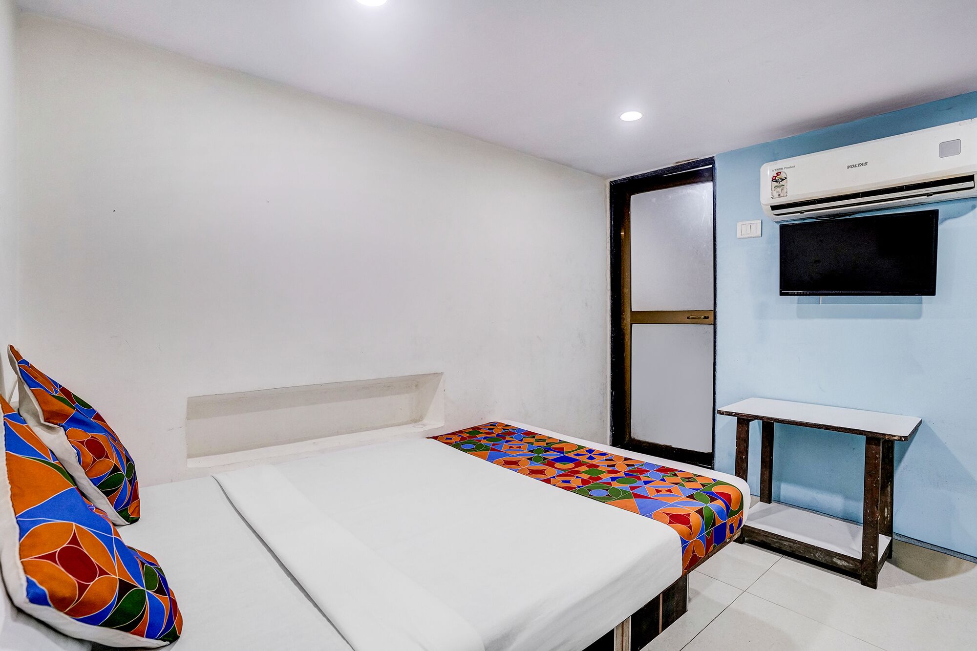 A room with a bed, a small table, an air conditioning unit, and a television.