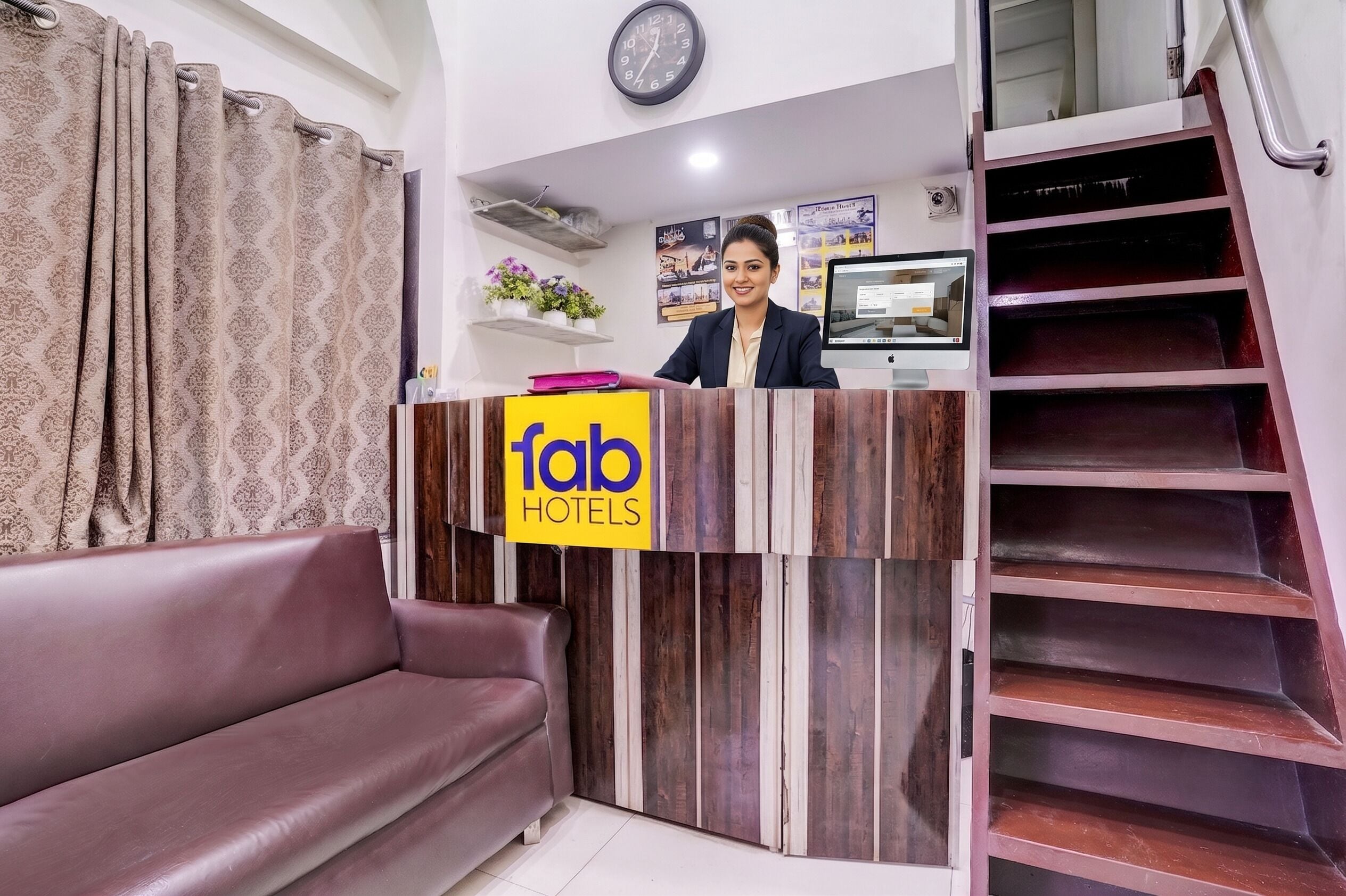Una recepción de hotel con un letrero que dice 'fab hotels', un monitor de computadora, un reloj y una escalera.