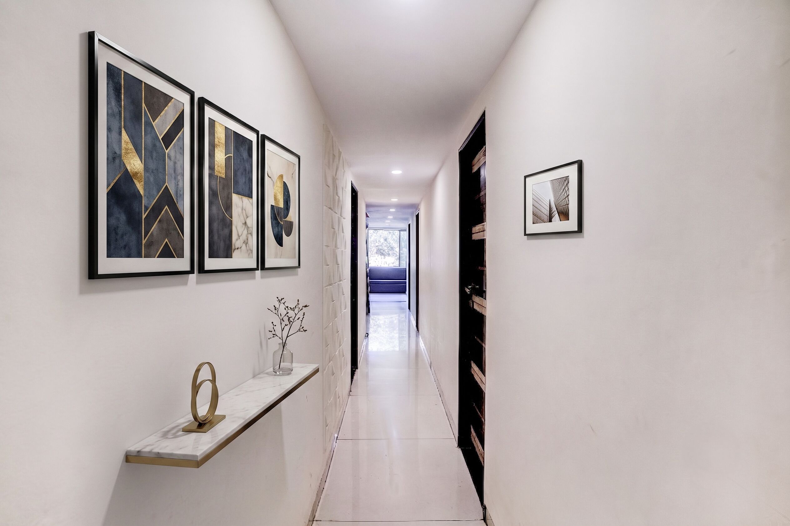 A hallway with a marble floor, a glass vase with branches, and framed abstract art on the walls.