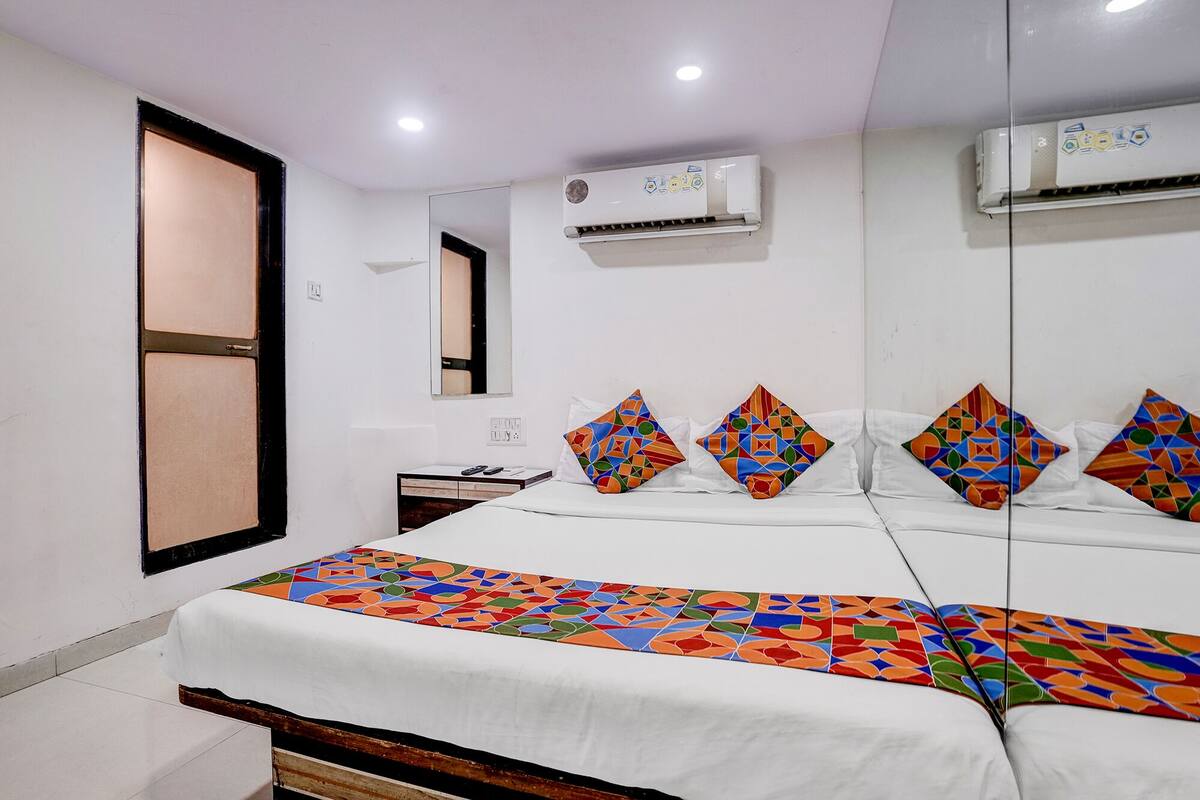 A hotel room with a bed, a bedside table, a mirror, and an air conditioning unit.
