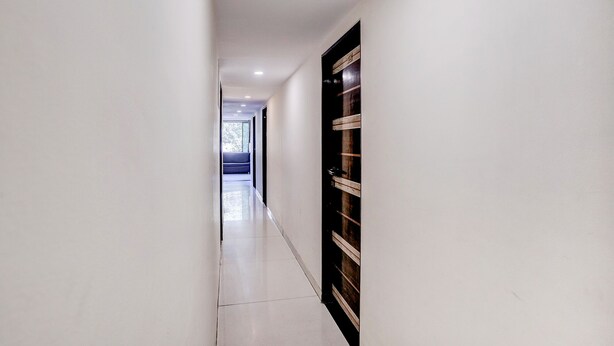 A hallway with a dark wooden door, white walls, and a tiled floor. - Fabhotel Blue Light (Mumbai)