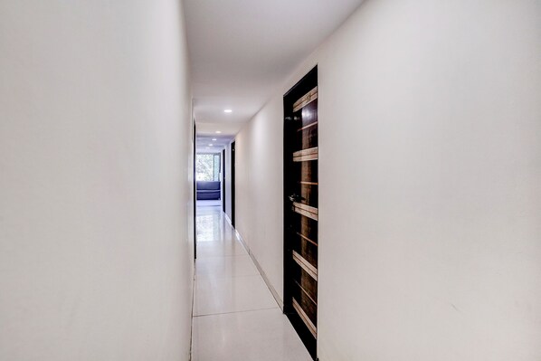 A hallway with a dark wooden door, white walls, and a tiled floor. - Fabhotel Blue Light (Mumbai)