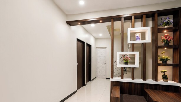 A modern hallway with a wooden bench, a staircase, and a wall-mounted shelf with flowers. - Fabhotel Aarvi Inn (Chhatrapati Sambhajinagar)