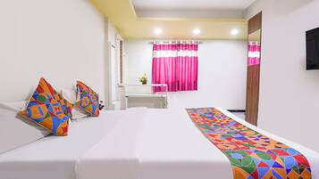 A hotel room with a bed, pillows, a window with curtains, a mirror, and a television.