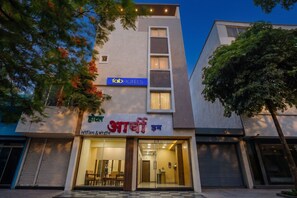 Een hotel met een moderne gevel, een herkenbaar bord met 'Fab Hotels' en een bord in de lokale taal dat 'Hotel' en 'Wasserij & Drogen' aangeeft.