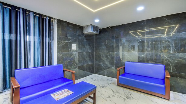 Een wachtruimte met twee blauwe fauteuils, een kleine tafel met een krant, en een plafond met geometrische verlichting.