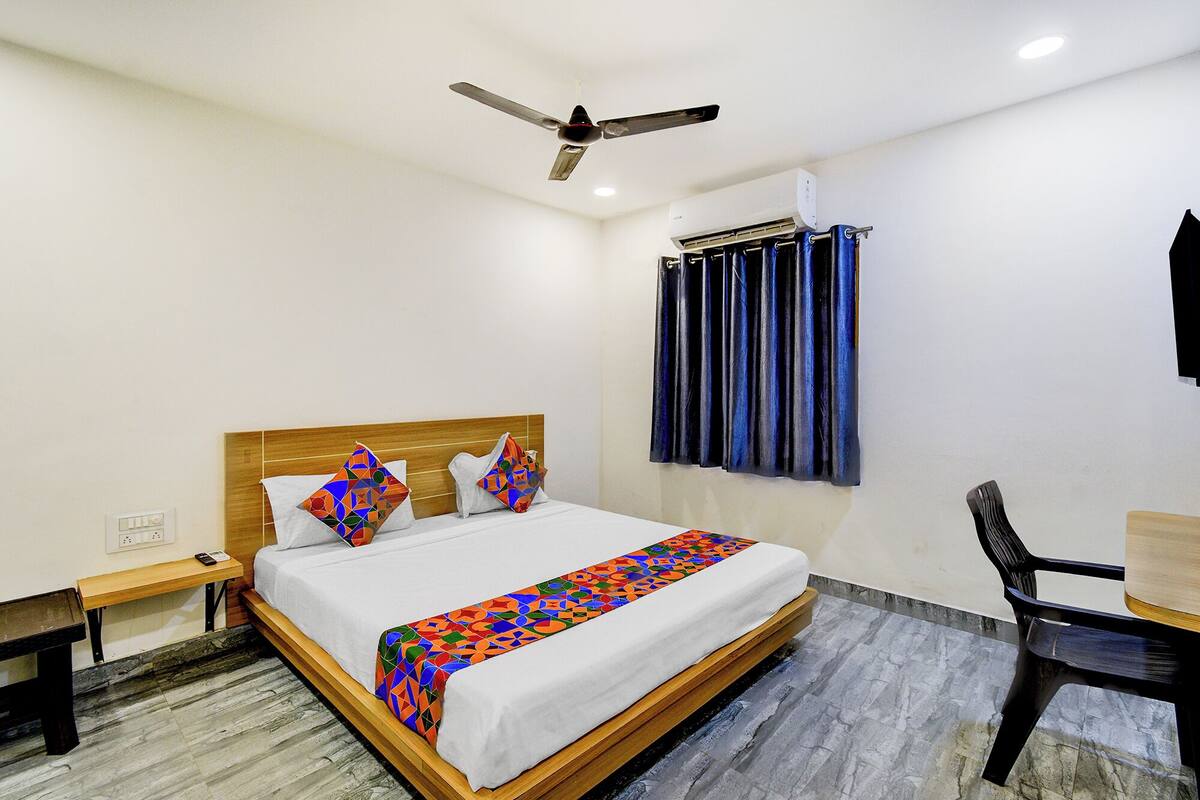 A hotel room with a bed, a desk, a chair, a ceiling fan, and an air conditioning unit.
