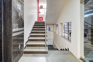 Una escalera con barandilla, una puerta roja en la parte superior y una ventana con celosía de metal en la pared.