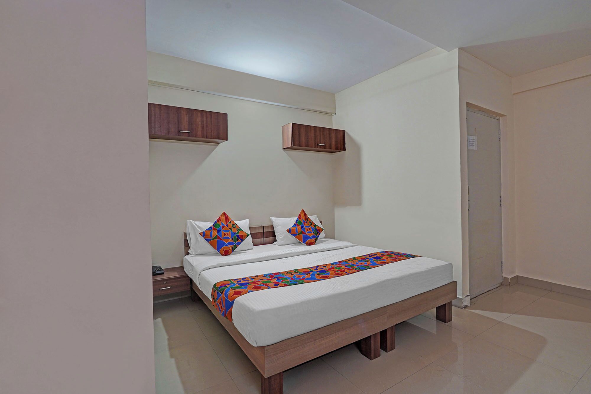 A bedroom with a bed, pillows, a nightstand, a wooden wardrobe, and a door.