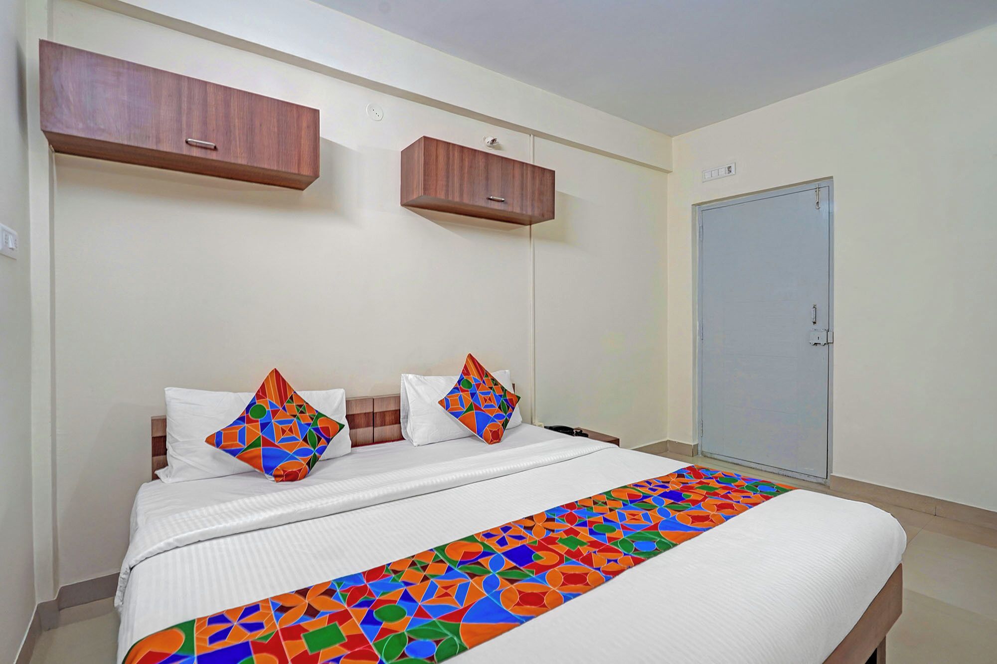 Una habitación de hotel con una cama, dos almohadas, una mesita de noche, un armario y una puerta.