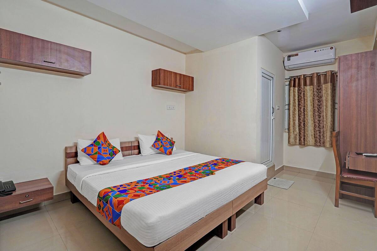 A bedroom with a bed, a bedside table, a wardrobe, an air conditioning unit, and a bathroom door.