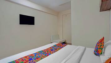 A hotel room with a bed, a small bedside table, a wall-mounted TV, and a colorful pillow.