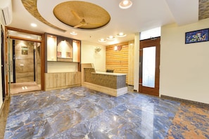 A hotel lobby with a reception desk, a wooden wall, a clock, and a ceiling fan. - FabHotel Prime Royal Elite - Nr Jaipur International Airport (Jaipur)