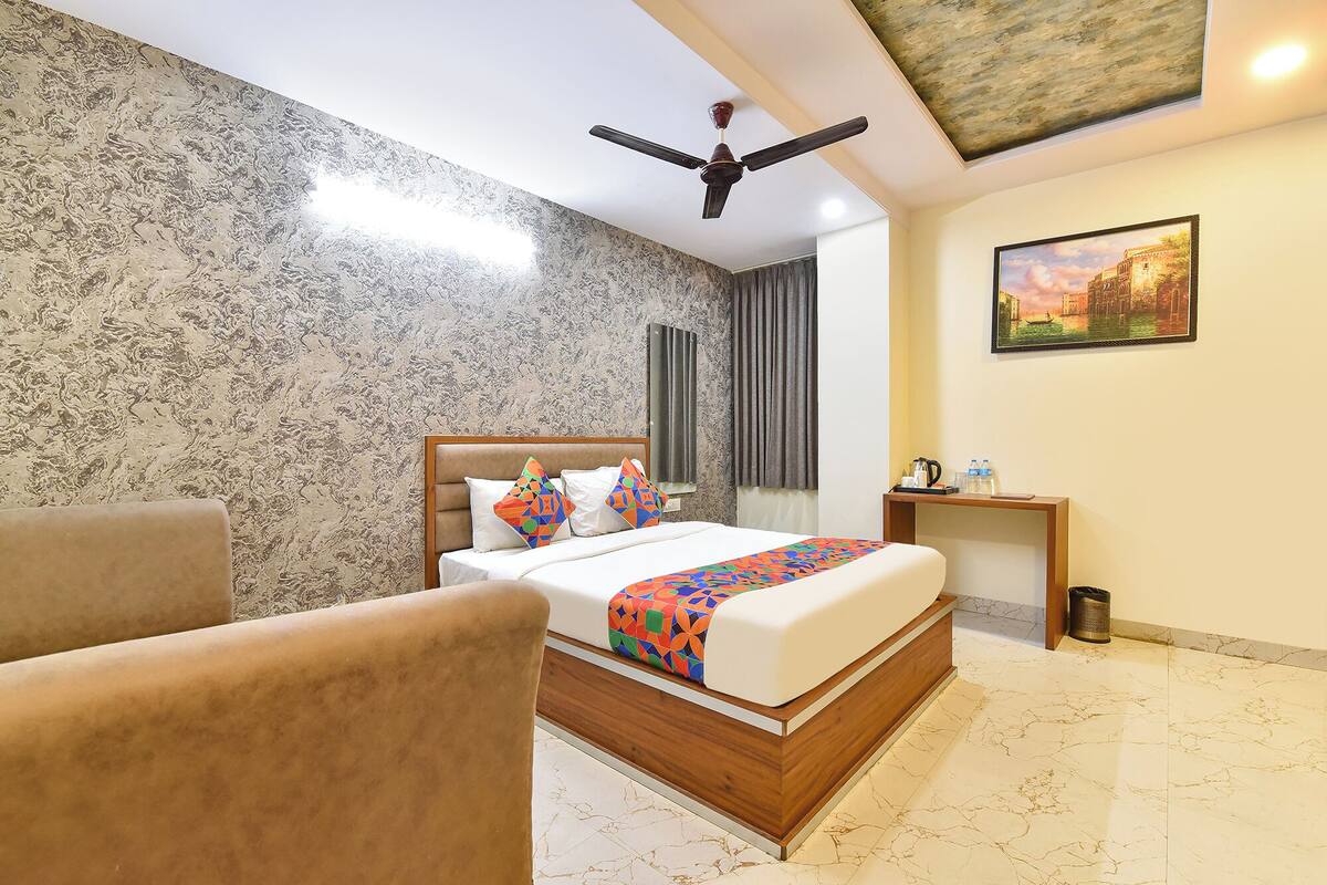 A hotel room with a bed, a chair, a ceiling fan, a nightstand, a painting, and a marble floor.