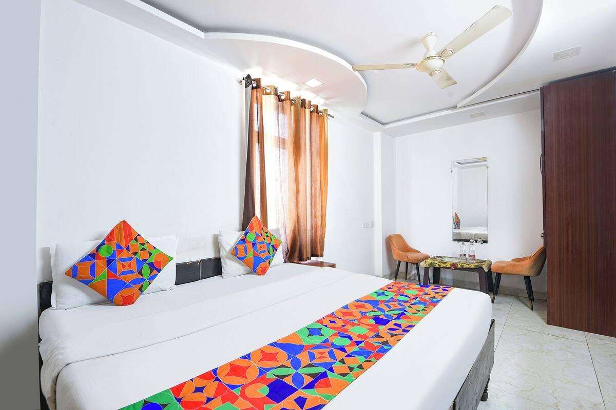 Habitación de hotel con cama, escritorio, silla, ventilador de techo y espejo.