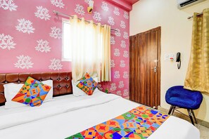 A bedroom with a bed, a wooden door, a blue chair, and a patterned wall. - FabHotel Chandra Dreams - 600m from Banaras Railway Station (Varanasi)
