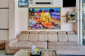Una sala de estar con un sofá, una mesa de centro de cristal y un cuadro enmarcado de un templo en la pared.