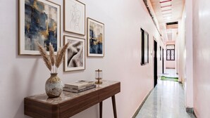 A hallway with framed artwork on the walls, a wooden console table with a vase and books, and a green mat on the floor. - FabHotel Chandra Dreams - 600m from Banaras Railway Station (Varanasi)