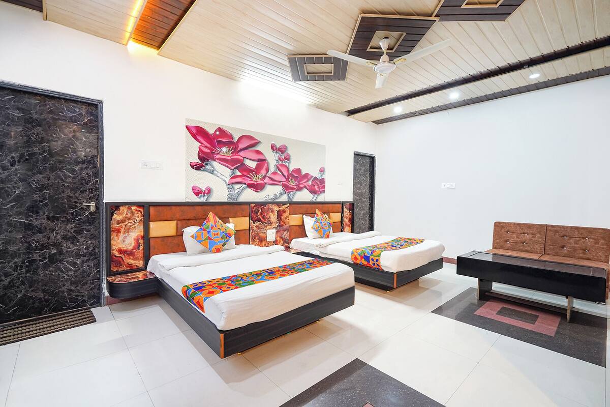Habitación de hotel con dos camas, un sofá, un ventilador de techo y una gran obra de arte floral en la pared.
