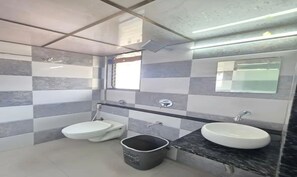 A bathroom with a toilet, bidet, sink, and a trash bin.