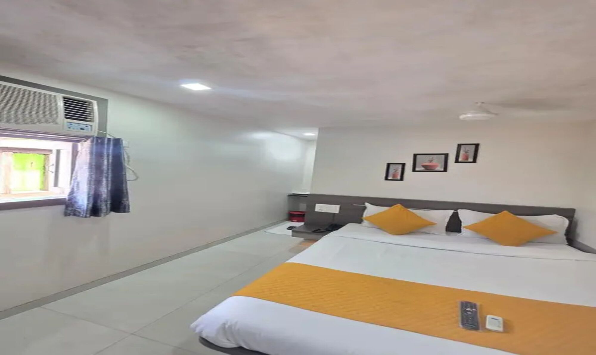 Una camera d'albergo con un letto, una finestra con tende, un condizionatore d'aria a muro e un piccolo tavolo con una sedia.