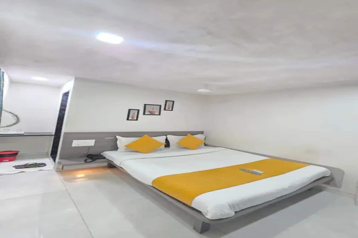 A hotel room with a bed, a bedside table, a mirror, and a wall-mounted picture.