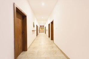 A hallway with wooden doors, a marble floor, and a sign for 'DAYAL ROOMS' in the distance. - FabHotel The Dayals & Lawns - Nr. Ayodhya Dham Bus Station (Faizabad)