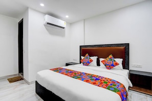 Een moderne hotelkamer met een groot bed, een hoofdeinde, een nachtkastje, een airconditioning en een houten deur.