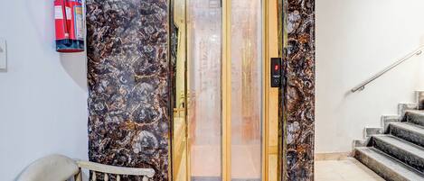 An elevator with a marble wall, a fire extinguisher, and a staircase.