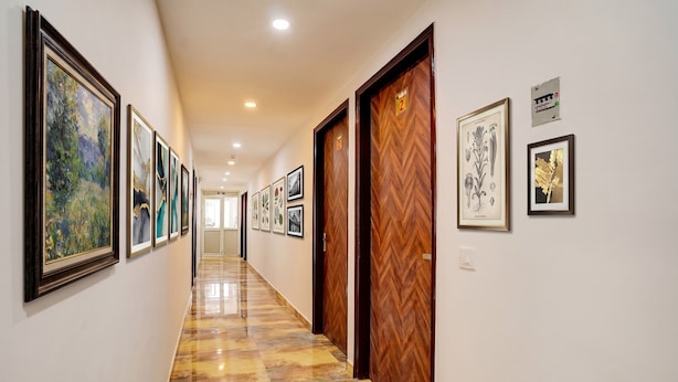 A hotel hallway with framed artwork on the walls, a polished floor, and wooden doors. - FabHotel Casa Royal - Greater Kailash (New Delhi)