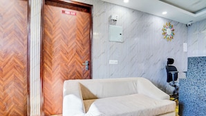 A room with a sofa, a chair, a fire exit sign, a wall-mounted light switch, and a decorative wall piece. - FabHotel Casa Royal - Greater Kailash (New Delhi)