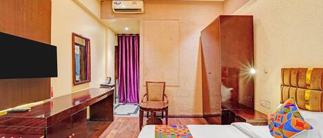 A hotel room with a bed, a desk, a chair, a television, and an air conditioning unit.