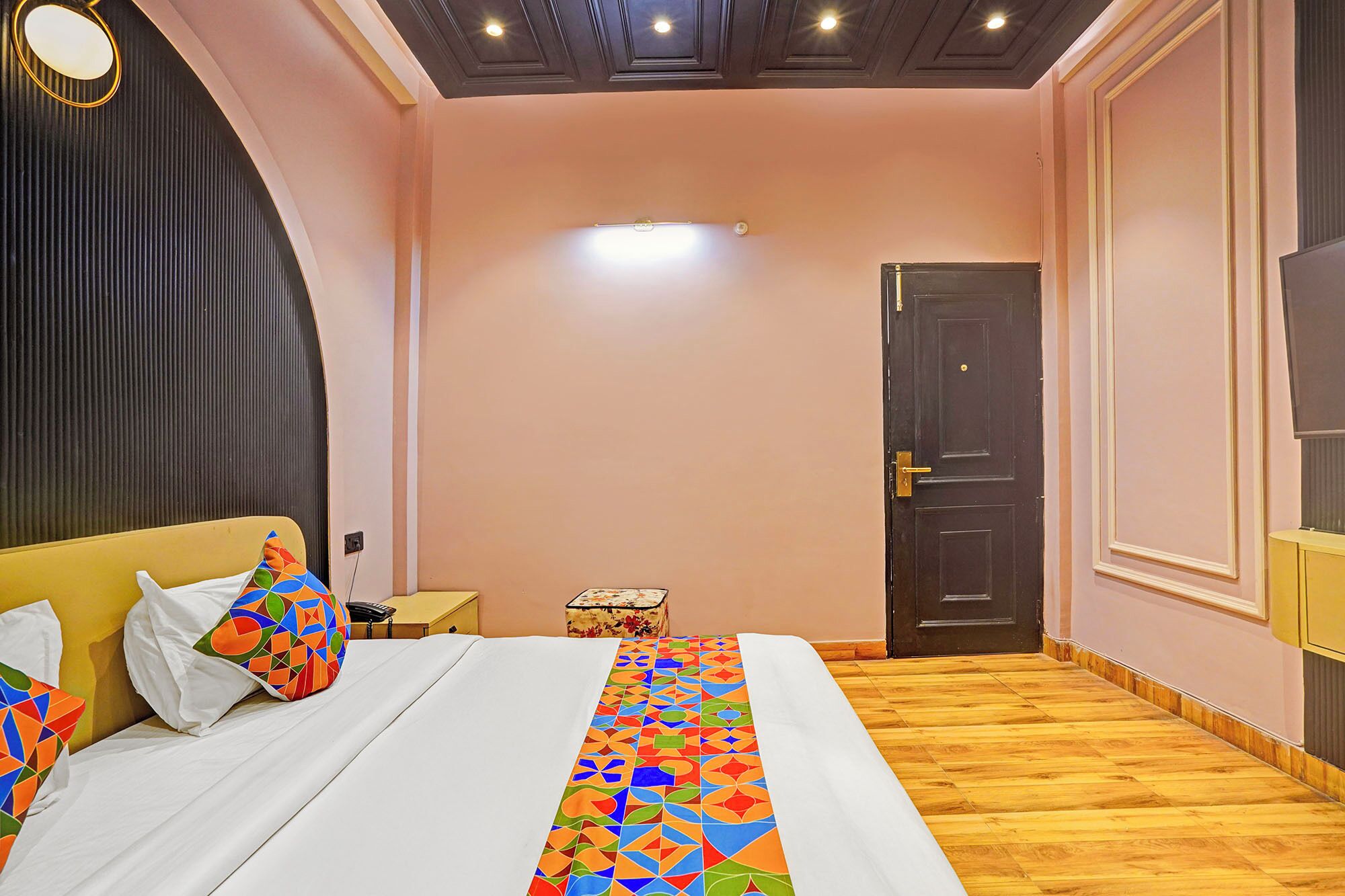 A bedroom with a bed, a bedside table, a nightstand, a door, and a wall-mounted light fixture.
