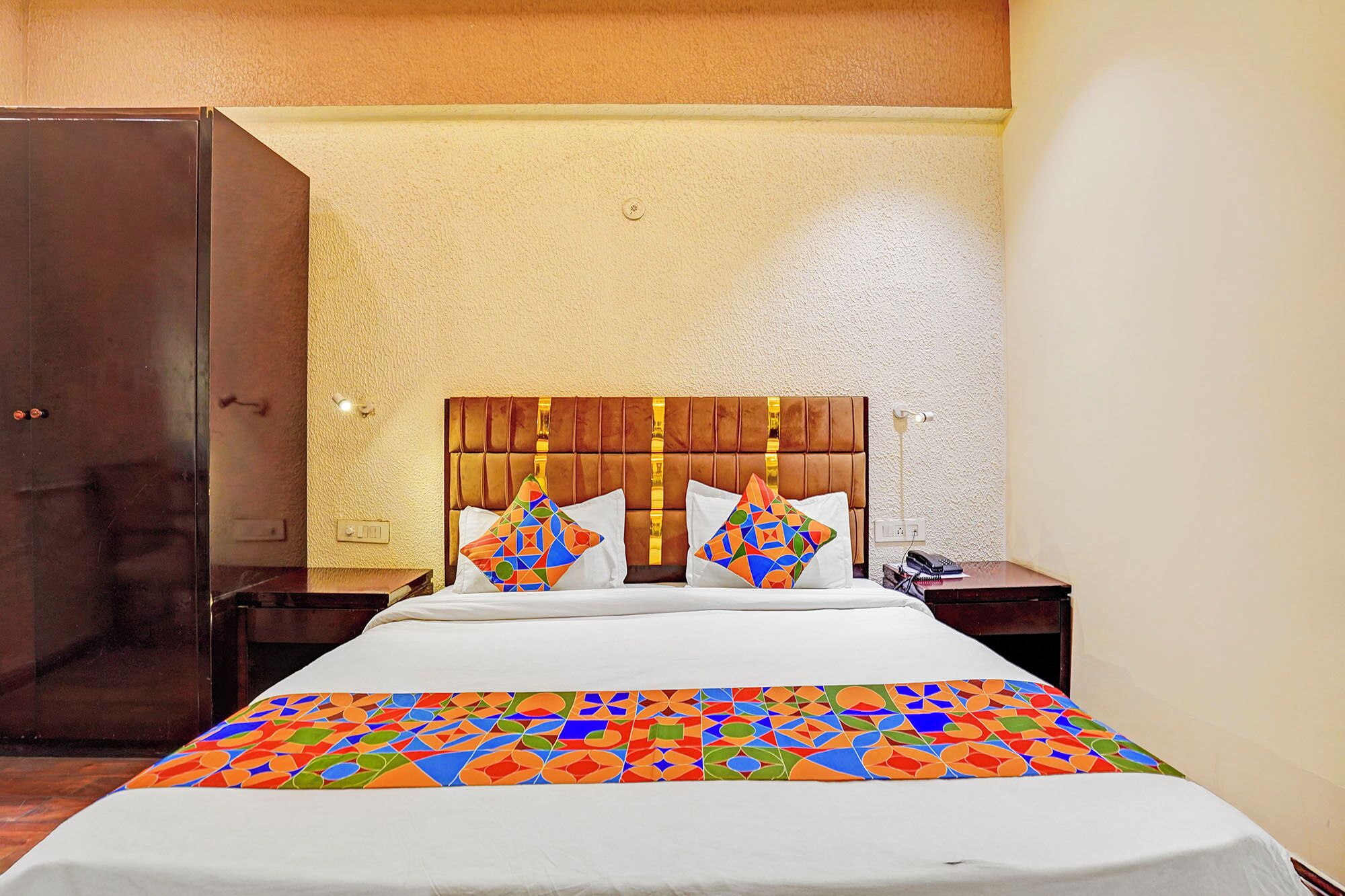 A hotel room with a bed, a nightstand, a telephone, and a wardrobe.